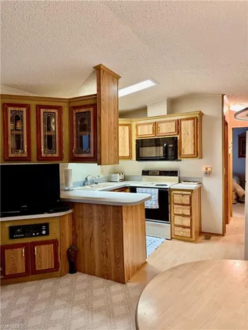 Kitchen featuring a peninsula, light countertops, white electric range, black microwave, and a textured ceiling