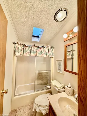 Full bath featuring vanity, a textured ceiling, shower / bath combination with glass door, and a skylight