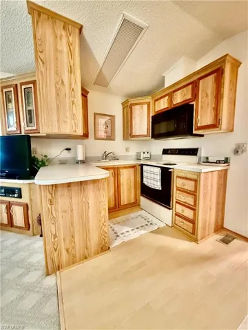 Kitchen featuring white electric range, light countertops, a textured ceiling, black microwave, and glass fronted cabinets