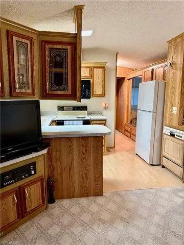 Kitchen featuring light countertops, a peninsula, white appliances, wood finish cabinetry, and light wood-style flooring