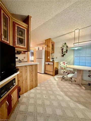 Kitchen featuring glass insert cabinets, wood finish cabinets, light countertops, freestanding refrigerator, and a textured ceiling