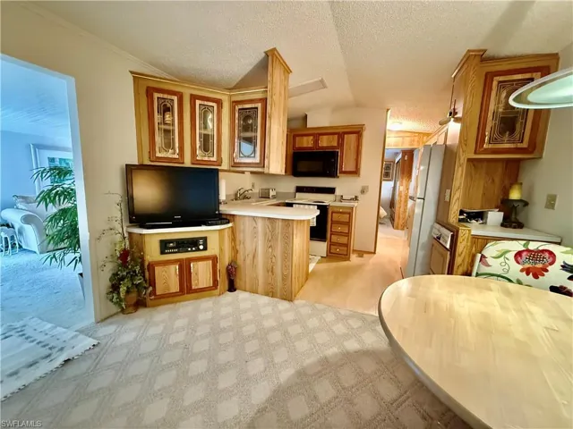 Kitchen with light countertops, glass insert cabinets, white appliances, a peninsula, and light colored carpet