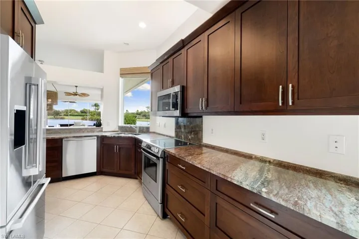 Kitchen with stainless steel appliances, dark stone counters, dark brown cabinets, light tile patterned flooring, and ceiling fan