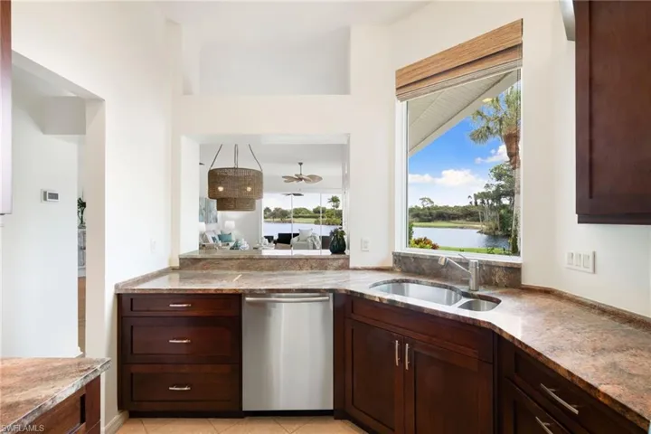 Kitchen with stainless steel dishwasher, dark brown cabinets, light stone counters, light tile patterned floors, and a water view