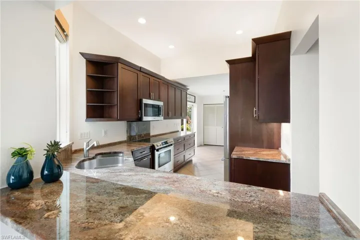 Kitchen with open shelves, dark brown cabinetry, stainless steel appliances, dark stone countertops, and recessed lighting