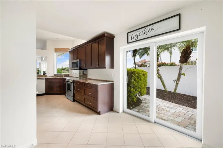 Kitchen with dark brown cabinets, light stone counters, appliances with stainless steel finishes, and light tile patterned floors
