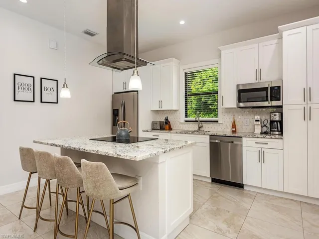 Kitchen with decorative backsplash, island exhaust hood, a center island, light stone countertops, and appliances with stainless steel finishes