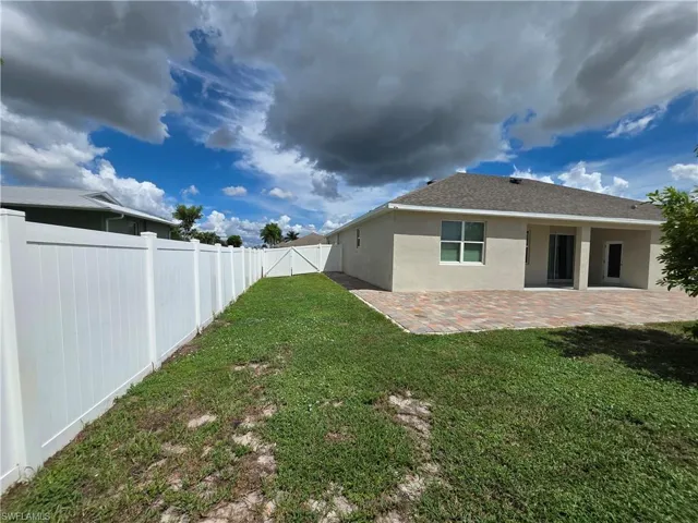 Expansive rear exterior featuring a paved patio area, white privacy fencing, and an accessible gate