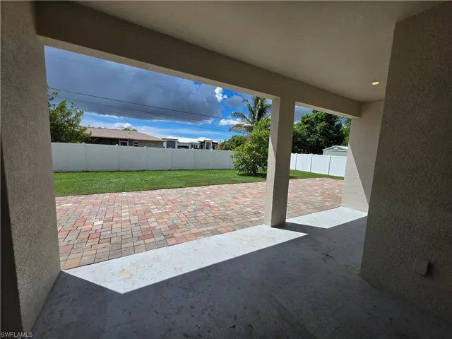 Covered patio with recessed lighting, concrete flooring, and stucco columns, overlooking a paver patio and lawn area
