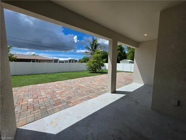 Covered patio with recessed lighting, concrete flooring, and a paver pathway leading to a grass area with a privacy fence