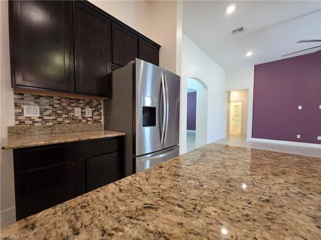 Kitchen featuring dark wood-finish cabinetry, granite countertops, tile backsplash, and a stainless steel refrigerator