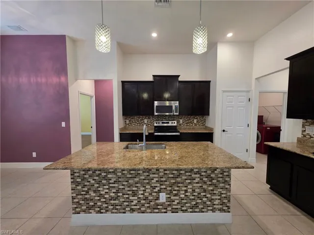 Kitchen featuring a tile backsplash, dark wood-finish cabinetry, granite countertops, and a central island with mosaic tile detailing