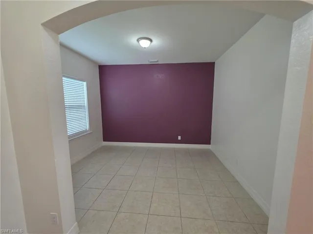 Archway entry leading to a room with tiled flooring, a window with blinds, and a distinct accent wall