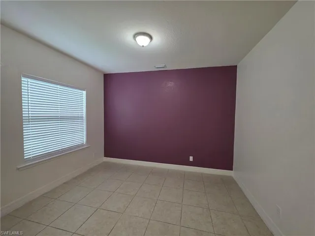 Neutral-toned tile flooring, flush-mount ceiling light fixture, window with blinds, and contrasting accent wall