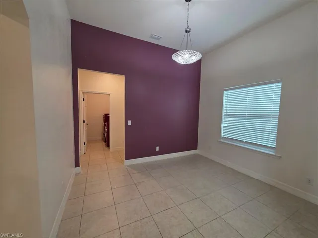 Vaulted ceiling, modern chandelier, tile flooring, interior window with blinds, and a distinctive accent wall