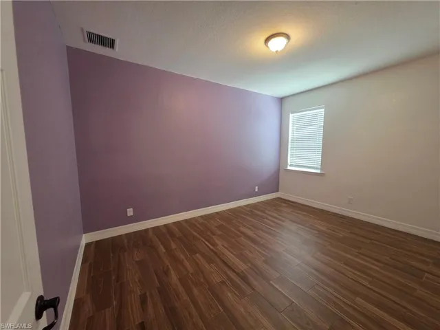 Wood-finish flooring, single window with blinds, white trim, and a ceiling-mounted light fixture