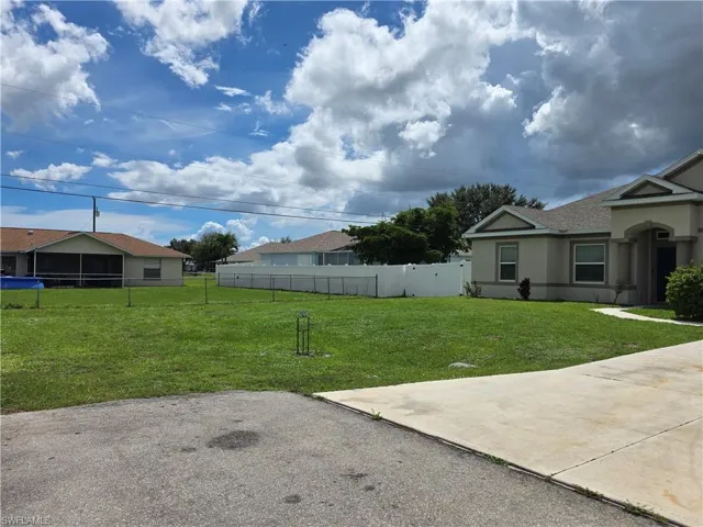 Expansive lot featuring a manicured lawn, paved driveway, and perimeter fencing