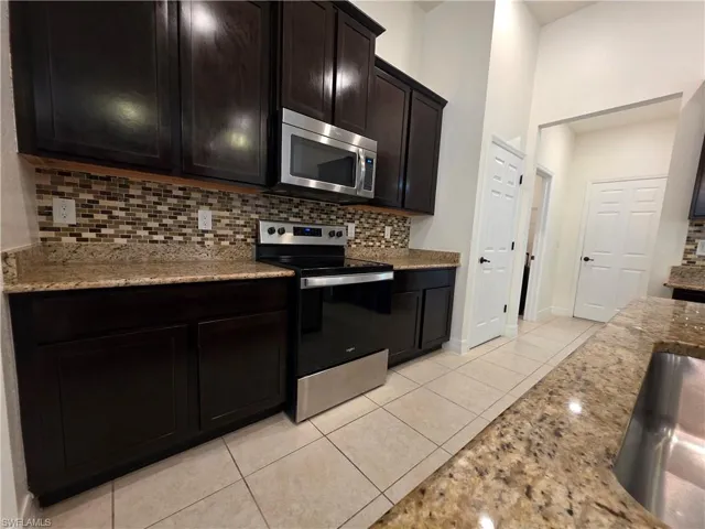 Dark wood-finish cabinetry, granite countertops, mosaic tile backsplash, stainless steel appliances, and tiled flooring