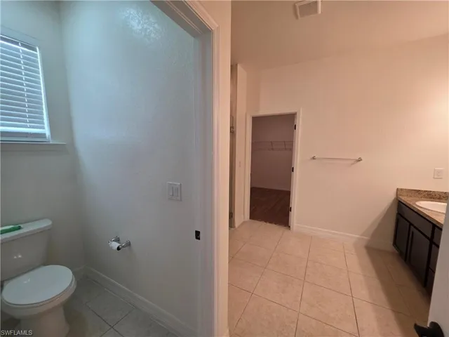 Tile flooring, built-in vanity with countertop and sink, window with blinds, and an open closet with wire shelving