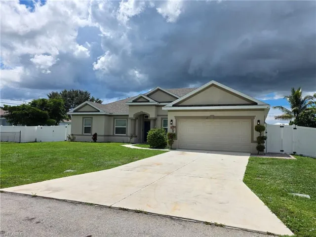 Stucco exterior with a pitched shingle roof, attached garage, concrete driveway, and white privacy fence
