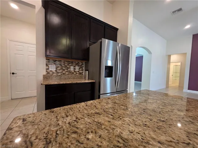 Kitchen featuring dark wood cabinetry, a mosaic tile backsplash, and a stainless steel refrigerator