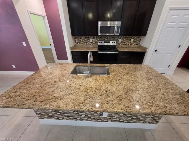 Kitchen featuring an expansive island with a stainless steel sink, tile mosaic island base, and stone countertops