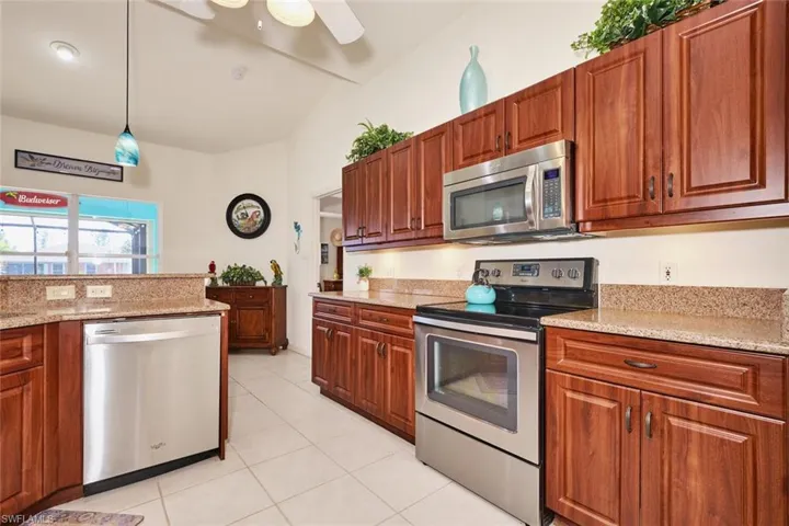 Kitchen with light tile patterned floors, a ceiling fan, stainless steel appliances, pendant lighting, and light stone counters