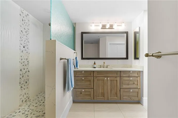 Bathroom featuring a wood-finish vanity with a single basin sink, white countertop, and a framed mirror