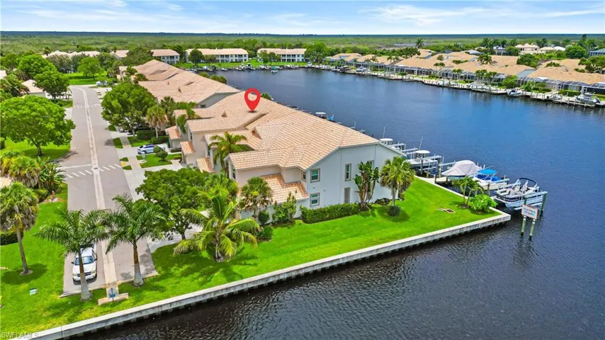 Waterfront property featuring a tile roof, mature palm trees, manicured lawn, and private boat docks