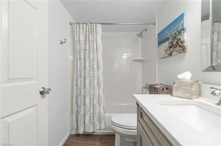 Full bathroom with hardwood / wood-style flooring, vanity, shower / bath combo, and toilet