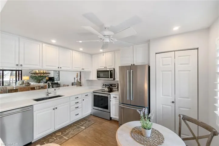 Kitchen with stainless steel appliances, white cabinets, sink, ceiling fan, and light wood-type flooring