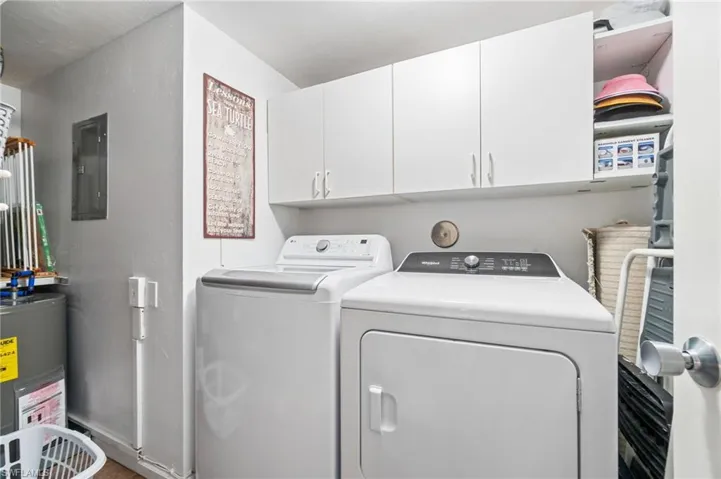 Clothes washing area with electric water heater, electric panel, cabinets, and washer and dryer