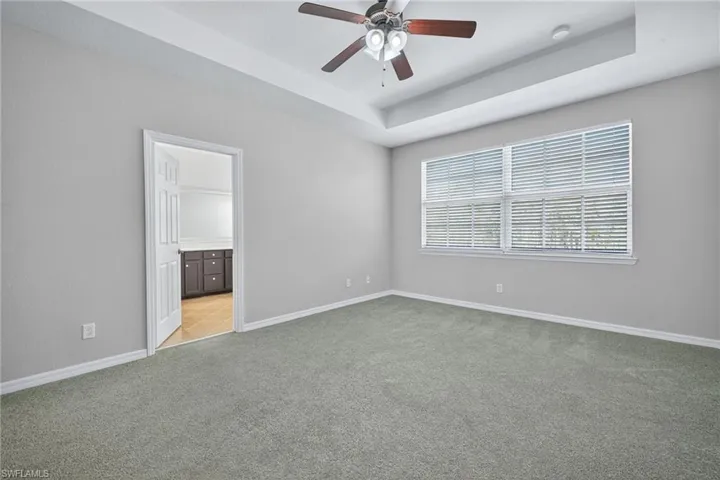 Unfurnished bedroom with a raised ceiling, light carpet, connected bathroom, and a ceiling fan