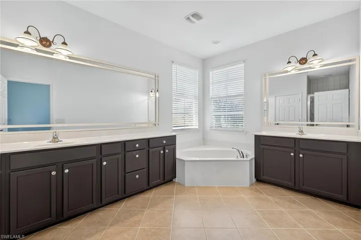 Bathroom featuring light tile patterned flooring, a bath, and two vanities