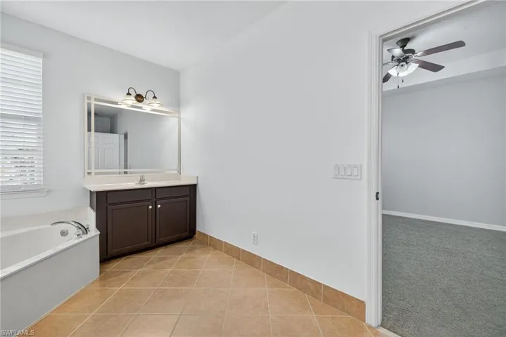 Bathroom featuring light tile patterned floors, vanity, a garden tub, and light colored carpet