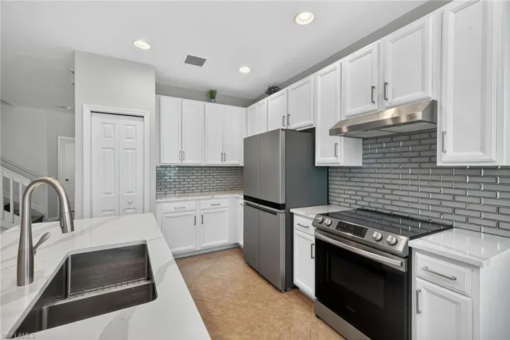 Kitchen with appliances with stainless steel finishes, white cabinets, under cabinet range hood, decorative backsplash, and recessed lighting
