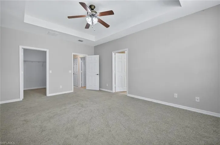 Unfurnished bedroom with a raised ceiling, a walk in closet, carpet flooring, and a ceiling fan
