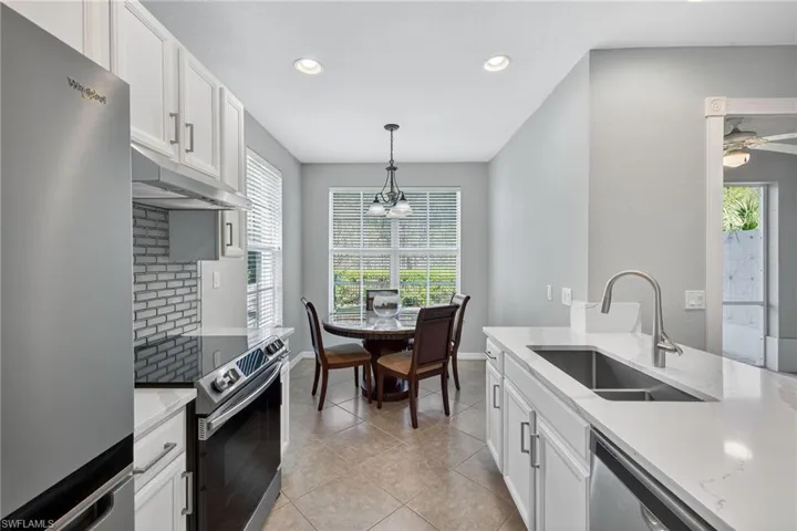 Kitchen with white cabinets, stainless steel appliances, light stone countertops, light tile patterned flooring, and hanging light fixtures