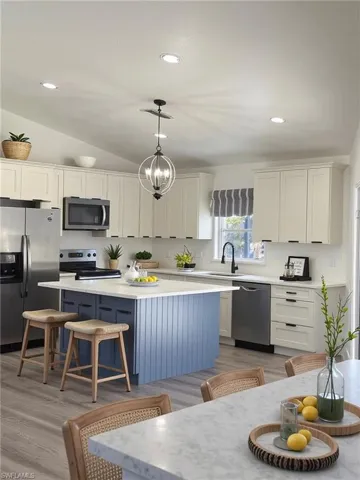 Kitchen featuring a breakfast bar area, stainless steel appliances, decorative light fixtures, white cabinets, and vaulted ceiling