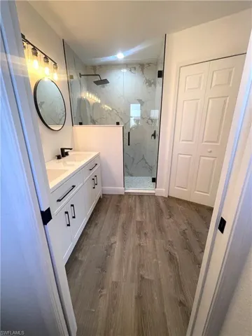 Full bathroom with double vanity, a marble finish shower, and dark wood-style floors