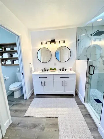 Full bathroom featuring double vanity, a marble finish shower, and light wood-type flooring