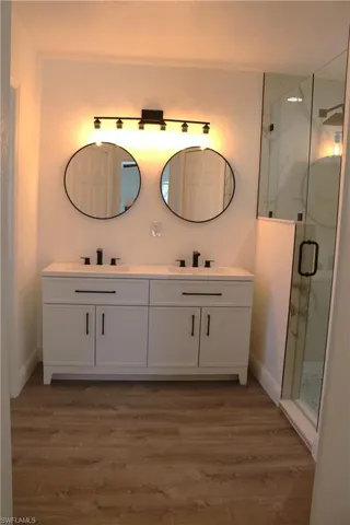 Bathroom with double vanity, a marble finish shower, and light wood finished floors