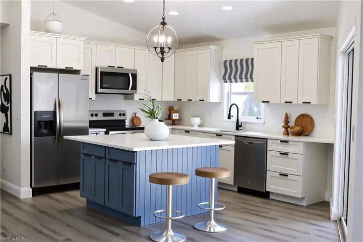 Kitchen with appliances with stainless steel finishes, blue cabinetry, white cabinetry, decorative light fixtures, and light wood-style flooring