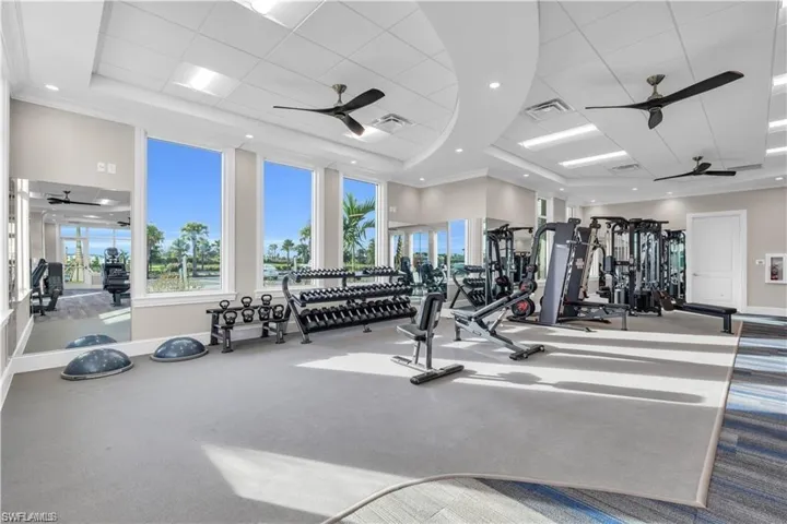 Gym with a raised ceiling, ceiling fan, and ornamental molding