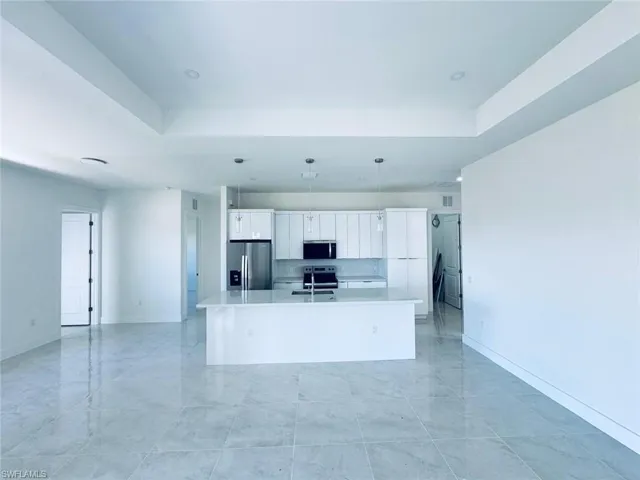 Kitchen featuring a sink, light countertops, appliances with stainless steel finishes, a raised ceiling, and a center island with sink