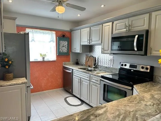 Kitchen with stainless steel appliances, gray cabinetry, light tile patterned floors, recessed lighting, and light stone counters