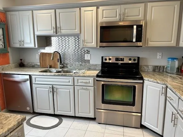 Kitchen with stainless steel appliances, light tile patterned floors, light stone countertops, decorative backsplash, and gray cabinets