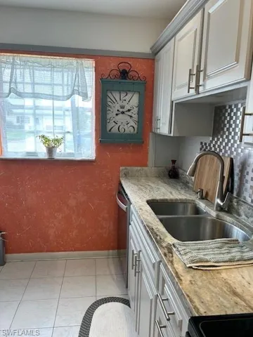 Kitchen with light tile patterned flooring, light stone counters, tasteful backsplash, range, and gray cabinetry