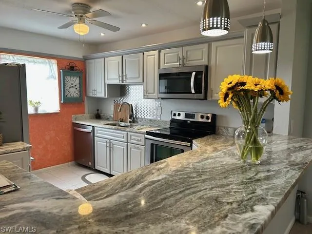 Kitchen featuring appliances with stainless steel finishes, light stone countertops, decorative light fixtures, light tile patterned floors, and recessed lighting