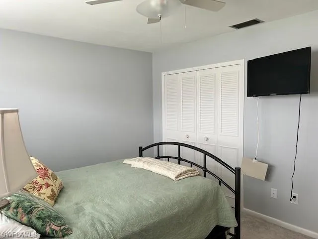 Carpeted bedroom with ceiling fan and a closet